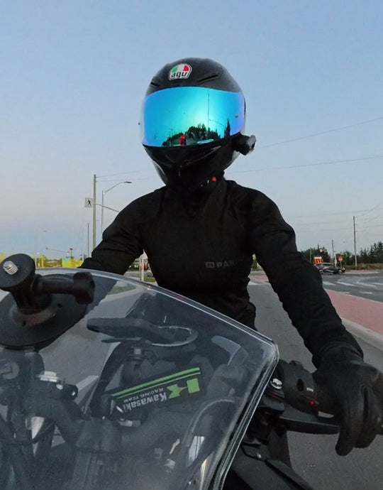 Motorcyclist in black gear and reflective blue visor helmet riding a sportbike, seen from the front.