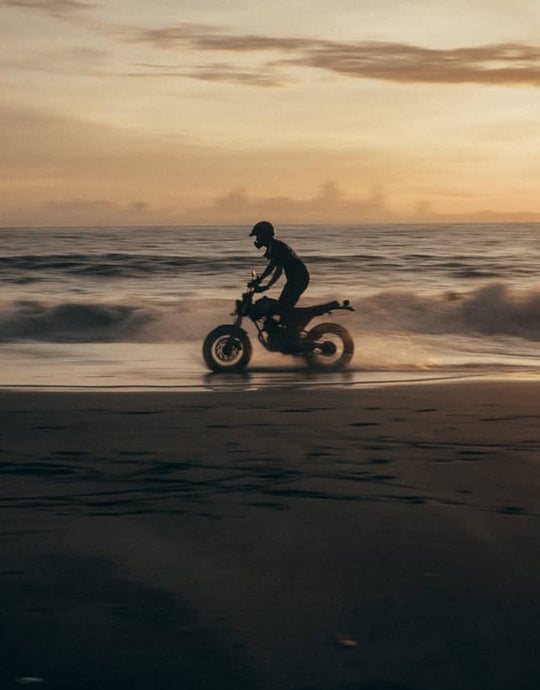 Motorcyclist riding alone at sunset along a beach or open road—evoking the feeling of a warm, comfortable summer ride.