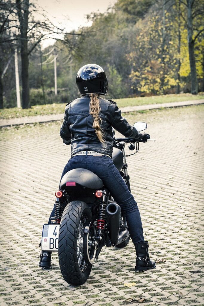 A blonde girl wearing Pando Moto Motorcycle jeans from the back on her Sportster